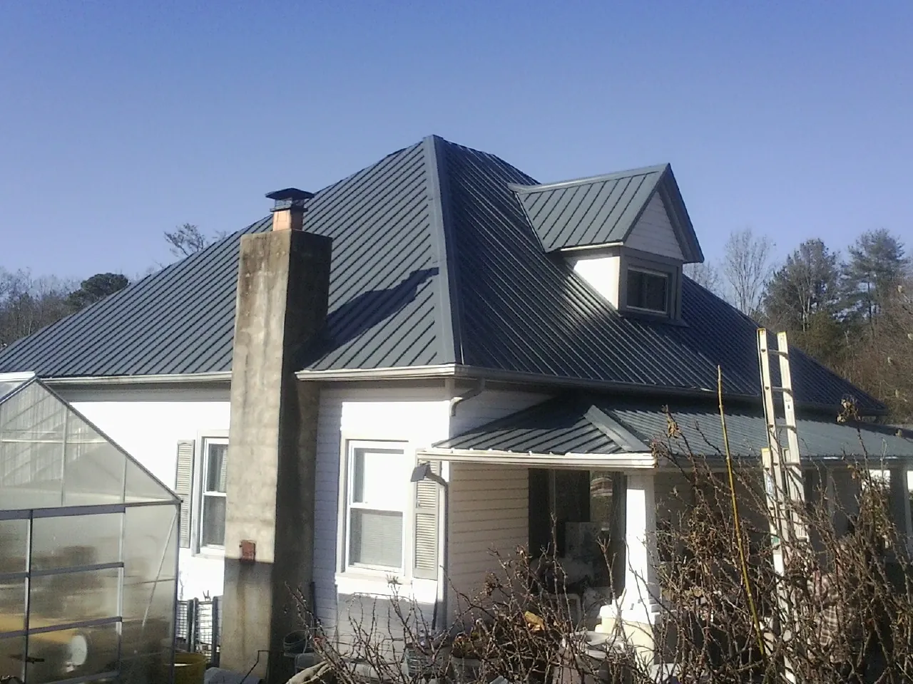 Dark blue standing seam metal roof on a white farmhouse with dormer — Slate & Tile Roof Repair by Roofing Brothers in Pall Mall