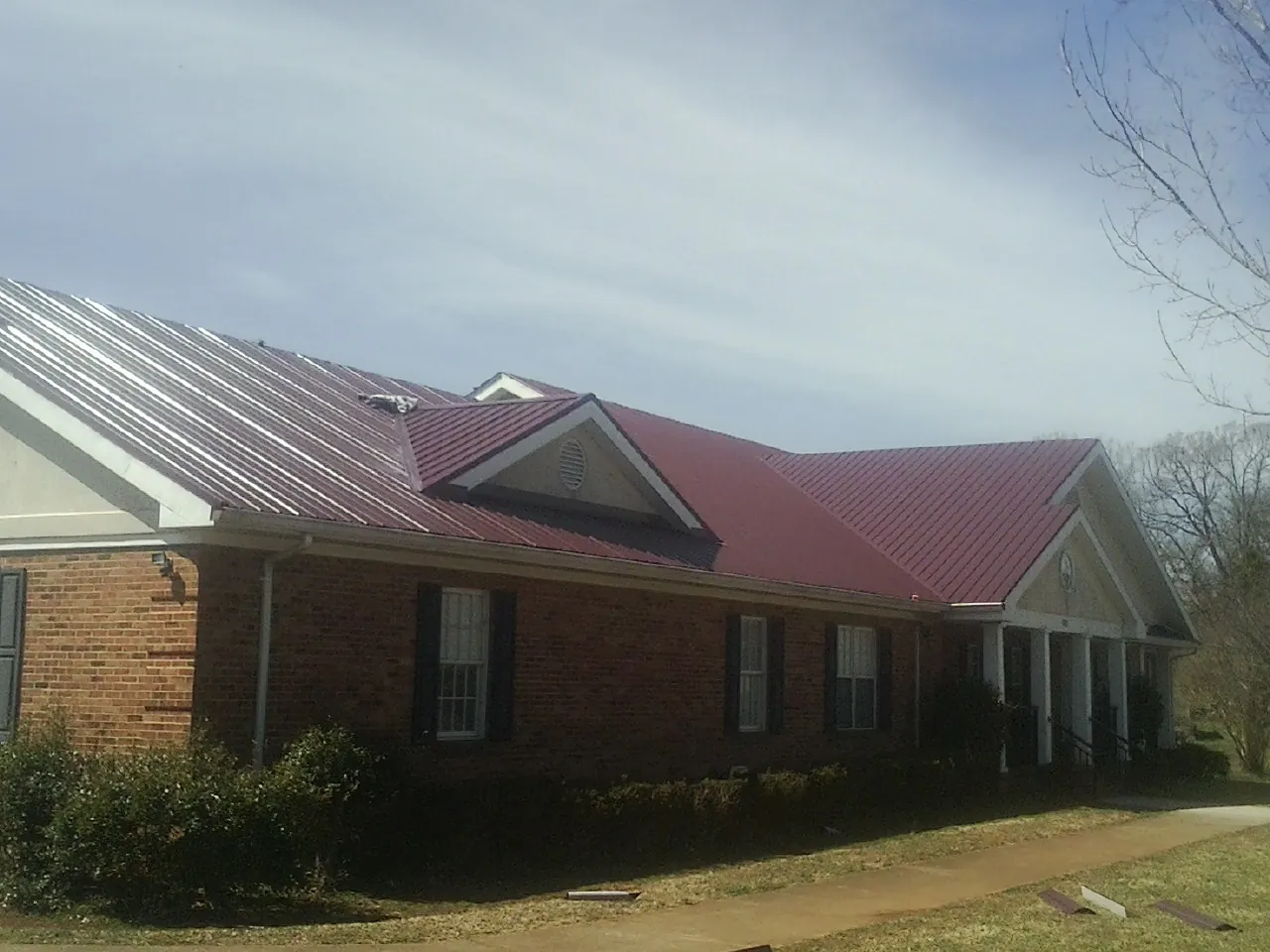 Red metal roof with gabled entries on a long brick building, from a Hail Damage Roof Repair job in Pall Mall