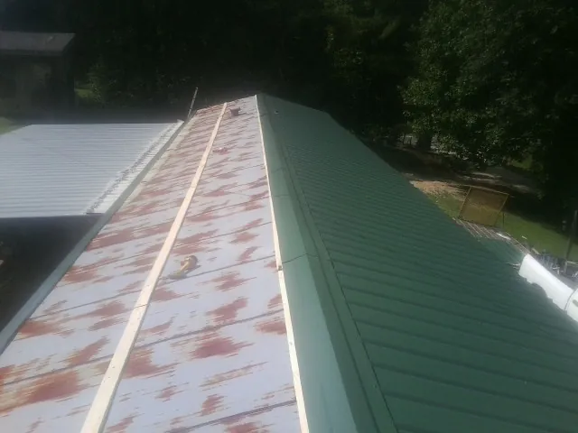 Old rusted panels beside newly installed green metal roofing — Wind Damage Roof Repair by Roofing Brothers in Pall Mall