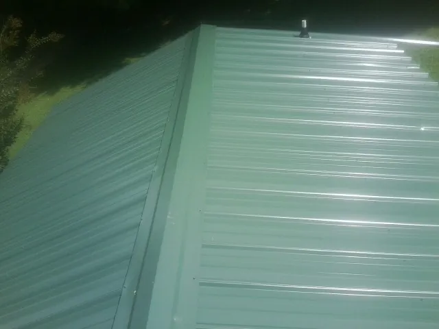 New green metal panels meeting at the ridge of a roof — Flat Roof Repair work by our crew in Pall Mall