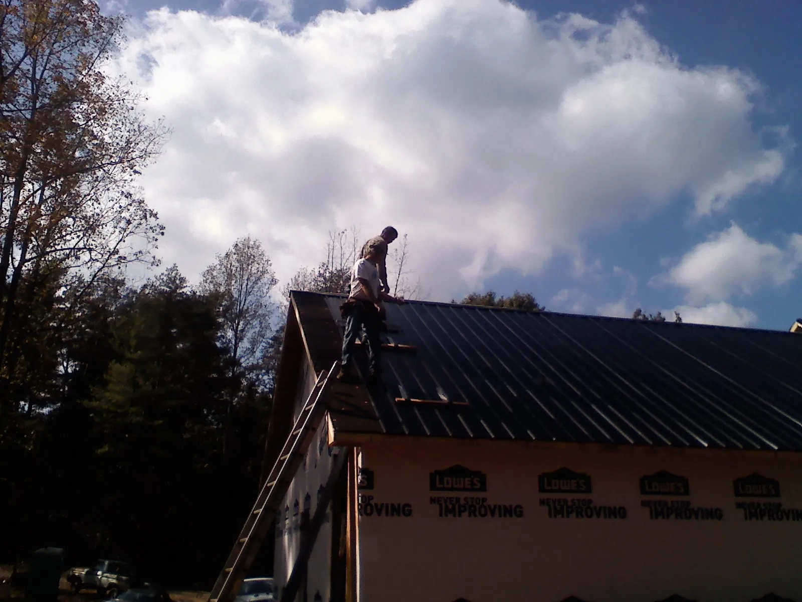Roofer fastening dark metal panels high against a cloudy sky, from a Roof Inspection job in Pall Mall