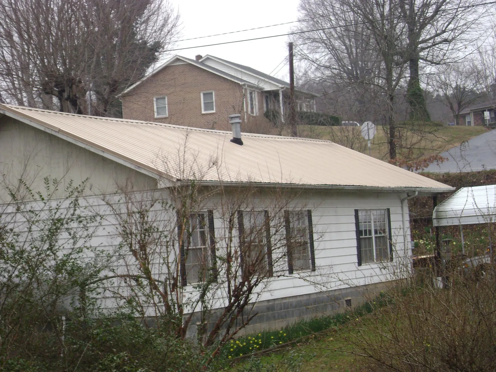 Tan metal roof on a white sided house set into a hillside — Commercial Roofing by Roofing Brothers in Pall Mall