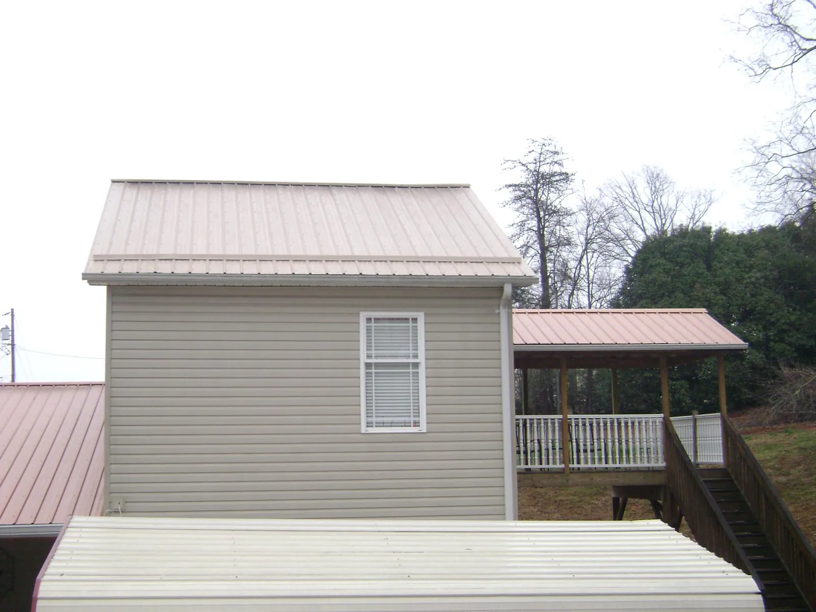 Tan metal roofs on a two story addition and attached porch, from a Roof Replacement job in Pall Mall